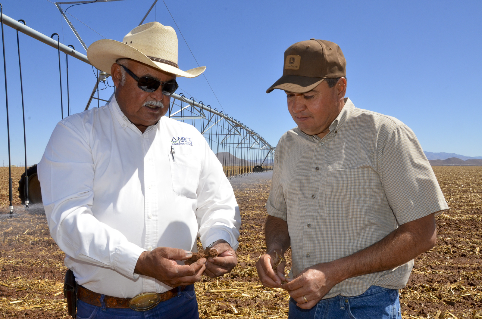 Two men on a recently harvested field in front of an irrigation boon.